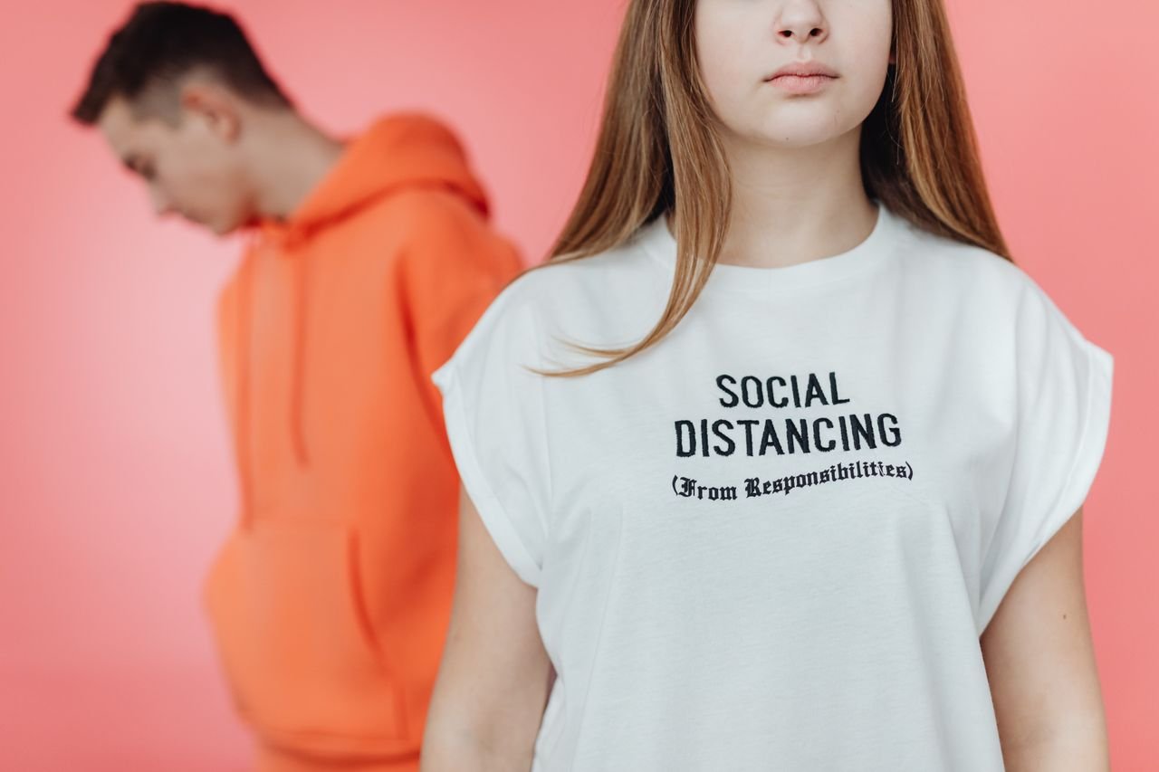 Young adults wearing trendy hoodies with a humorous social distancing message on a blurred background.