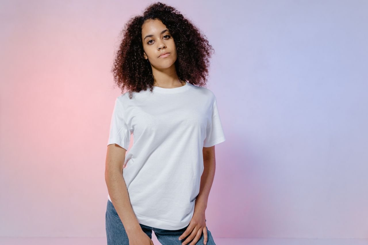 Portrait of a confident woman with curly hair in a casual white t-shirt against a soft color background.